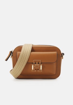 Bruine leren crossbodytas met beige gevlochten band en goudkleurig logo op voorvak tegen een witte achtergrond.