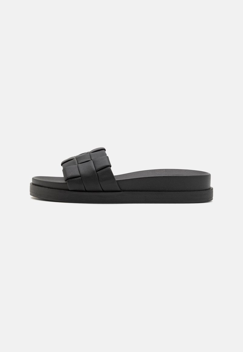 Sandale à glissière noire avec un design de sangle tissée, semelle plate et finition mate lisse. Construction légère et style minimaliste.