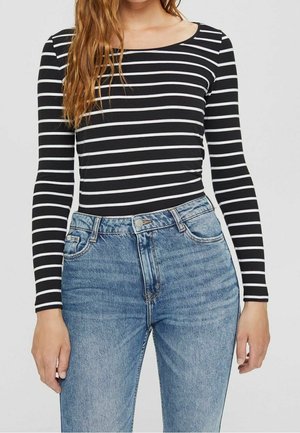 Maglione a maniche lunghe a righe bianche e nere abbinato a jeans azzurri a vita alta, con dettagli in denim classici e una silhouette aderente.