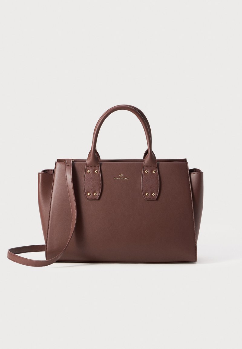 Bruine leren handtas met dubbele bovenhandvatten, een verstelbare schouderriem, hardware in goudkleur en een gestructureerde vorm. Elegante merkdetails zijn aanwezig.