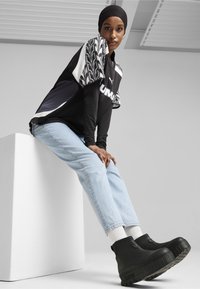 Zwart-wit sporttop met patroon mouwen, lichtblauwe jeans en zwarte plateau laarzen. Glad stof met gestructureerde accenten.
