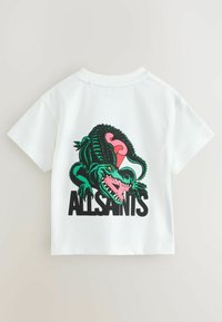 Valge puuvillasest t-särgist, millel on rohelise krokodilliga graafika roosa aksendiga ja musta teksti "ALLSAINTS" seljal. Lühikesed varrukad, ümar kaelus.