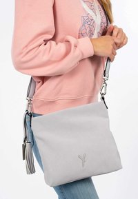 Borsa a spalla grigia perforata con una texture liscia, cinturino nero regolabile e un tassello decorativo; presenta un sottile dettaglio del logo.
