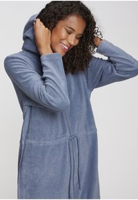 Hooded blue fleece robe with full zipper, textured fabric, drawstring waist, and side pockets, showcasing a comfortable, relaxed fit.