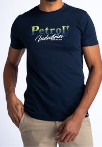 Tmavě modré bavlněné tričko s přechodovým bílým a zeleným grafikým logem "Petrol Industries". Klasický kulatý výstřih, krátké rukávy.