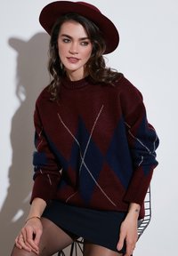 Bordo in mornarsko modra argyle vzorec pleten pulover z okroglim izrezom in oversize krojem, v kombinaciji s temnim krilom.
