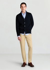 Cardigan côtelé marine, boutonné, porté sur une chemise rayée bleu clair, associé à un pantalon beige et des mocassins brun foncé.