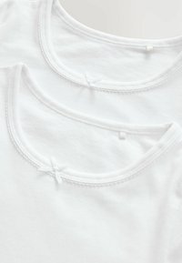 Två vita bomull t-shirts med rund halsringning, dekorerade med detaljerad sömnad och små rosetter i mitten av varje halsringning.