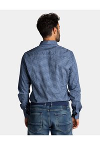 Blauw gemusterd shirt met lange mouwen, voorzien van kleine cirkelontwerpen en een button-down kraag. Gecombineerd met blauwe denim jeans.
