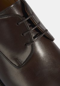 Chaussure habillée en cuir marron avec une texture lisse, un bout arrondi et un laçage à quatre œillets. Présente des détails cousus près des lacets.