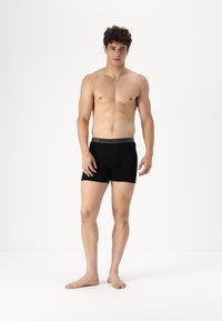 Fekete boxer alsónadrág szürke "ICEBREAKER" derékkal. Puha textúra, közepes combhossz, testhezálló fazon. A modell mezítláb áll, kezét az oldalán tartja.