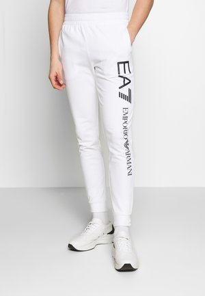 White sweatpants with elastic waistband, ribbed cuffs, and printed black text "EA7 EMPORIO ARMANI" along the left leg.