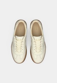 Ténis de couro creme com acabamento texturizado, apresentando sola de borracha castanha, biqueira redonda e design clássico com atacadores.