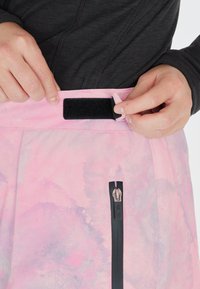 Helle rosa Hose mit Aquarellmuster. Verfügt über eine schwarze Reißverschlusstasche und einen Klettverschlussbund für eine verstellbare Passform. Weicher Stoff.