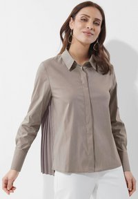 Helle beige Langarmbluse mit Kragen, Knopfleiste vorne und gefälteltem Stoffdetail am Rücken. Glatte Textur.