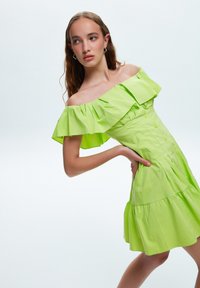 Vestido sin hombros de algodón en un vibrante color verde lima, con mangas acampanadas, botón frontal y una falda en capas con una silueta acampanada.