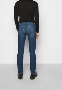 Blå denimjeans med rak benform, med medelhög midja, bakfickor och en slät yta. Bärs med en svart långärmad tröja.