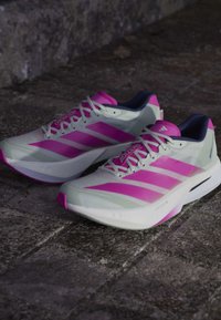 Par hvide og pink Adidas Adizero løbesko placeret på en tekstureret stensurface.