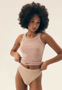 Jasnoróżowy, prążkowany top na ramiączkach z szerokimi ramiączkami i okrągłym dekoltem, w zestawie ze współczesnymi, beżowymi majtkami bikini o wysokim stanie.