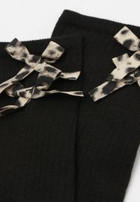 Calze nere lavorate a maglia con due fiocchi in stampa leopardata beige e nera nella parte superiore, con una texture a coste e una finitura liscia.