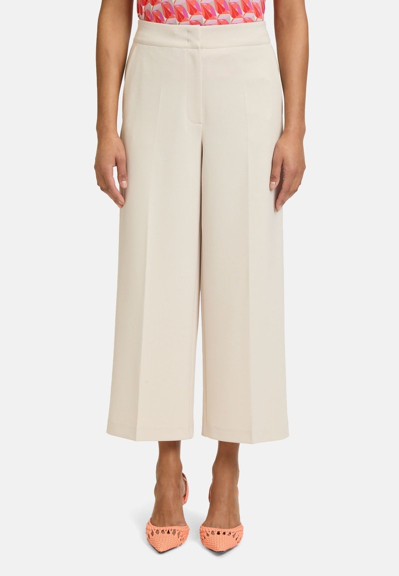 Vita byxor i en ljus beige tyg, med hög midja och skarpa veck. Matchade med texturerade skor i korallfärg.