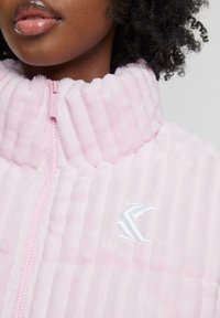 Giacca rosa con zip realizzata in tessuto morbido e texturizzato con strisce verticali. Presenta un colletto alto e un logo bianco ricamato sul lato.