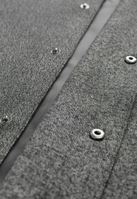 Cămășă butonată din material textil gri, țesut, cu capse argintii, având un finisaj texturat și o căptușeală interioară netedă în contrast.