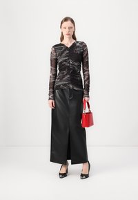 Čierny oversized top s dlhým rukávom a textúrovaným dizajnom skombinovaný s čiernou koženou maxi sukňou s predným rozparkom a červenou taškou. Čierne lodičky.