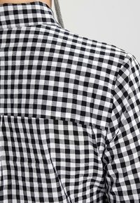 Svartvit rutig skjorta med klassisk krage, mjuk textur och yoke-detalj på baksidan samt en enkel ficka.