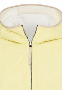 Żółta kurtka z centralnym zamkiem błyskawicznym i beżowym obszyciem, z miękkim, białym kołnierzem wyłożonym polarem dla zapewnienia ciepła.