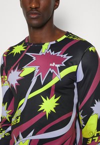 Schwarzes Langarmshirt mit auffälligem, buntem Grafikdesign, das grüne, lila und kastanienbraune Explosionen sowie Textakzente zeigt. Elastisches Material.