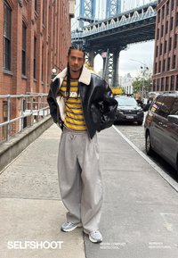 Black leather bomber jacket with a white shearling collar, yellow and brown striped shirt, gray wide-leg sweatpants, and gray sneakers.
