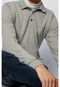 Grå långärmad polo med krage och tre knappar, som har subtil  brodyr av logotypen på bröstet och ett mjukt, texturerat tyg.