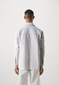 Witte en grijs gestreepte lange mouwen shirt met een knoopdown-kraag, zijspleten en subtiele textuur, gecombineerd met off-white broeken.