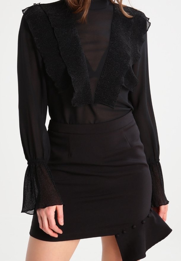 Outfit nero composto da una blusa trasparente con scollo arricciato e maniche lunghe texturizzate, abbinato a una minigonna aderente con dettagli ai bottoni.