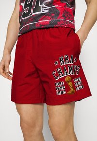 Röda shorts med texten "NBA CHAMPS" och en trofé grafik, med åren 1991-1998 tryckta bredvid. Lättviktigt material och elastisk midja.