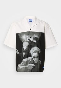 Κοντομάνικο πουκάμισο με ασπρόμαυρη γραφική εκτύπωση τριών φιγούρων. Άσπρο πάνω ύφασμα, μαύρο κάτω τμήμα. Στυλ με κουμπιά μπροστά.