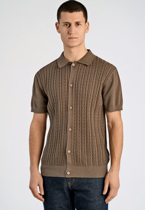Polo tricot à manches courtes marron avec un motif en relief de câbles, doté d'un col et d'une fermeture à boutons sur le devant. Assorti à un jean en denim foncé.