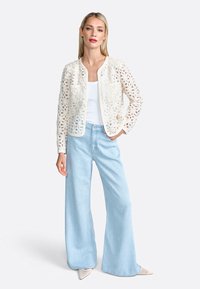 Cardigan bianco all'uncinetto con motivi floreali, abbinato a jeans a gamba larga blu chiaro e scarpe beige con punta.