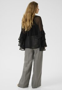 Blusa nera trasparente con maniche a volant abbinata a pantaloni larghi a quadri grigi. Il tessuto morbido e il taglio ampio enfatizzano il comfort.