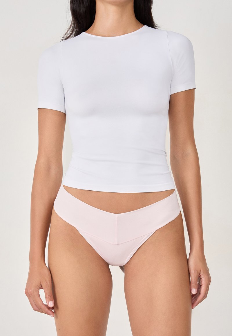 Haut blanc à manches courtes et culotte rose. Le haut est ajusté avec un col rond ; la culotte a une taille en forme de V et un design sans coutures.