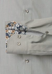 Męska koszula z guzikami w cienkie pionowe paski, złożony rękaw odsłaniający wewnętrzną mankiet w kwiatowy wzór.