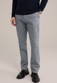 Šviesiai pilki tekstūruoti kelnės su laisvu siluetu, pasižyminčios subtiliu raštu. Suderintos su juodais loaferiais ir tamsiai mėlynu megztiniu.