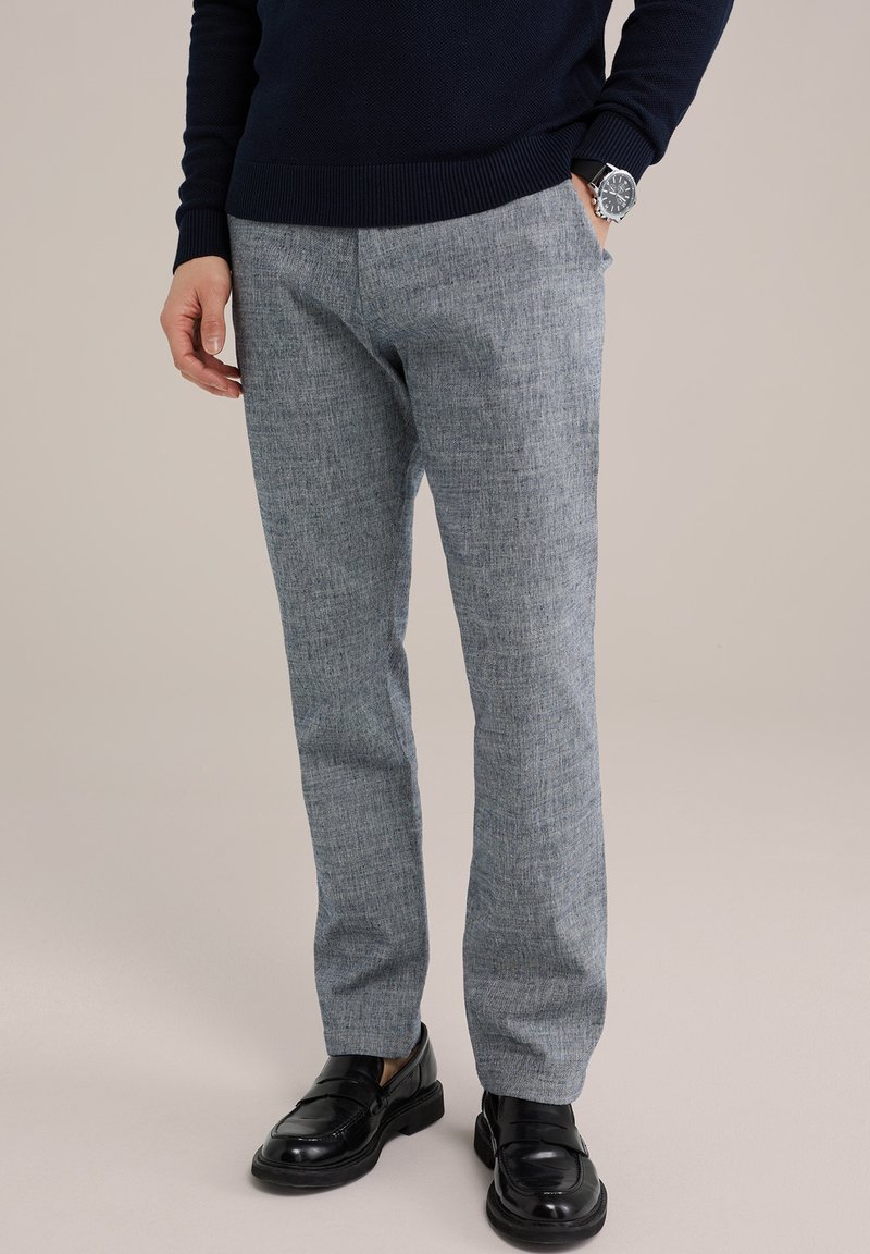 Šviesiai pilki tekstūruoti kelnės su laisvu siluetu, pasižyminčios subtiliu raštu. Suderintos su juodais loaferiais ir tamsiai mėlynu megztiniu.