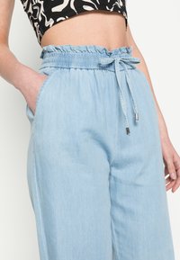 Light blue, relaxed-fit pants with an elastic waistband, drawstring detail, and side pockets. Fabric has a smooth texture.