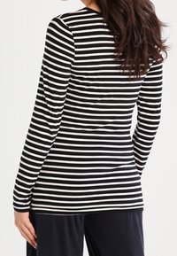 Kvinna iklädd en åtsittande svart och vit horisontellt randig långärmad tröja, sedd bakifrån.