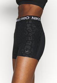 Gros plan sur un vêtement de sport montrant un short noir Nike Pro avec un imprimé léopard discret et un logo Nike Swoosh brillant sur la cuisse.
