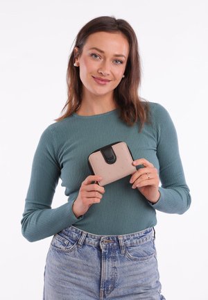 Small pink wallet with embossed dots, black closure, and rounded edges, held by a person wearing a teal ribbed top and denim shorts.