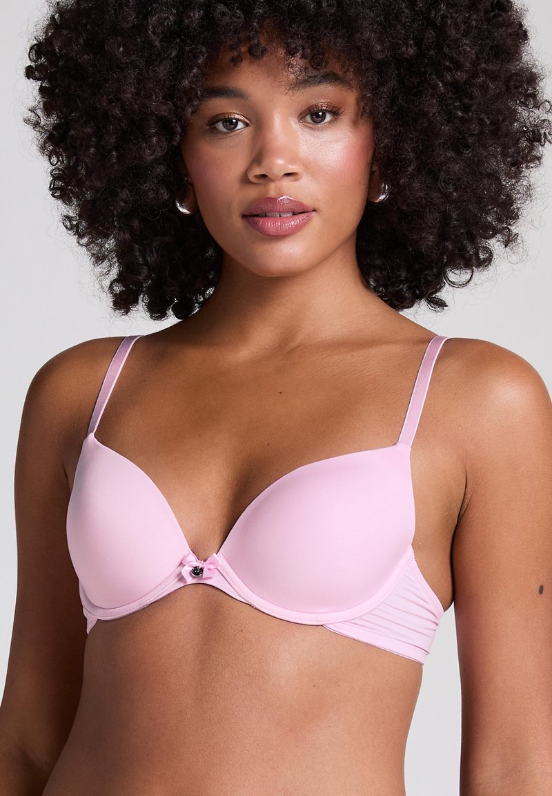 Reggiseno imbottito rosa chiaro con spalline regolabili, caratterizzato da un dettaglio a fiocco centrale e tessuto morbido, che offre una silhouette liscia.