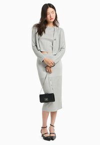 Crop top a coste grigio e gonna coordinata, abbinati a un cappotto sartoriale, completati con una borsa nera e tacchi a caviglia neri.